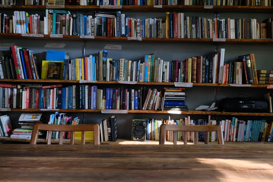 E-reader with text displayed next to a stack of physical books on a wooden table.